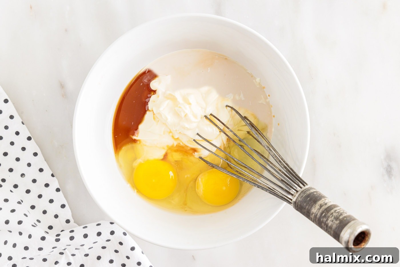 whisking eggs, milk, mayonnaise, and vanilla in abowl