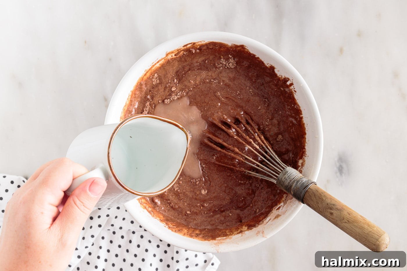 adding hot water to chocolate cake batter in a bowl