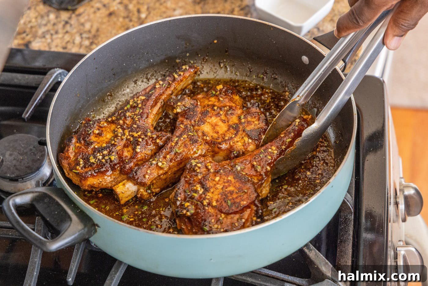 Using tongs to flip veal chops, ensuring they are evenly coated in the aromatic pan sauce.