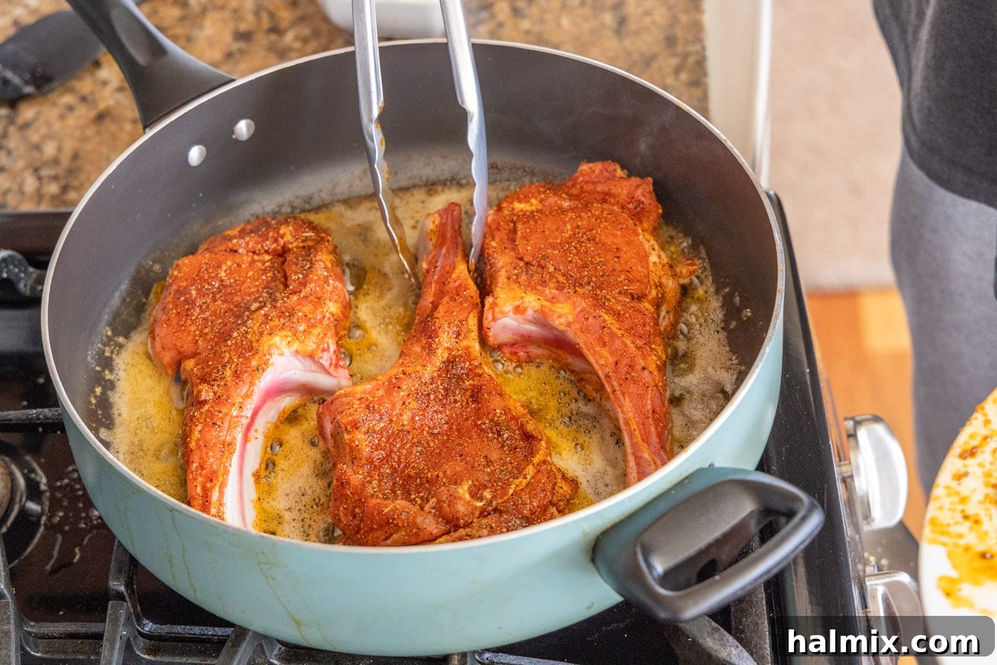 Veal chops searing in a hot skillet with melted butter, showing a developing golden crust.