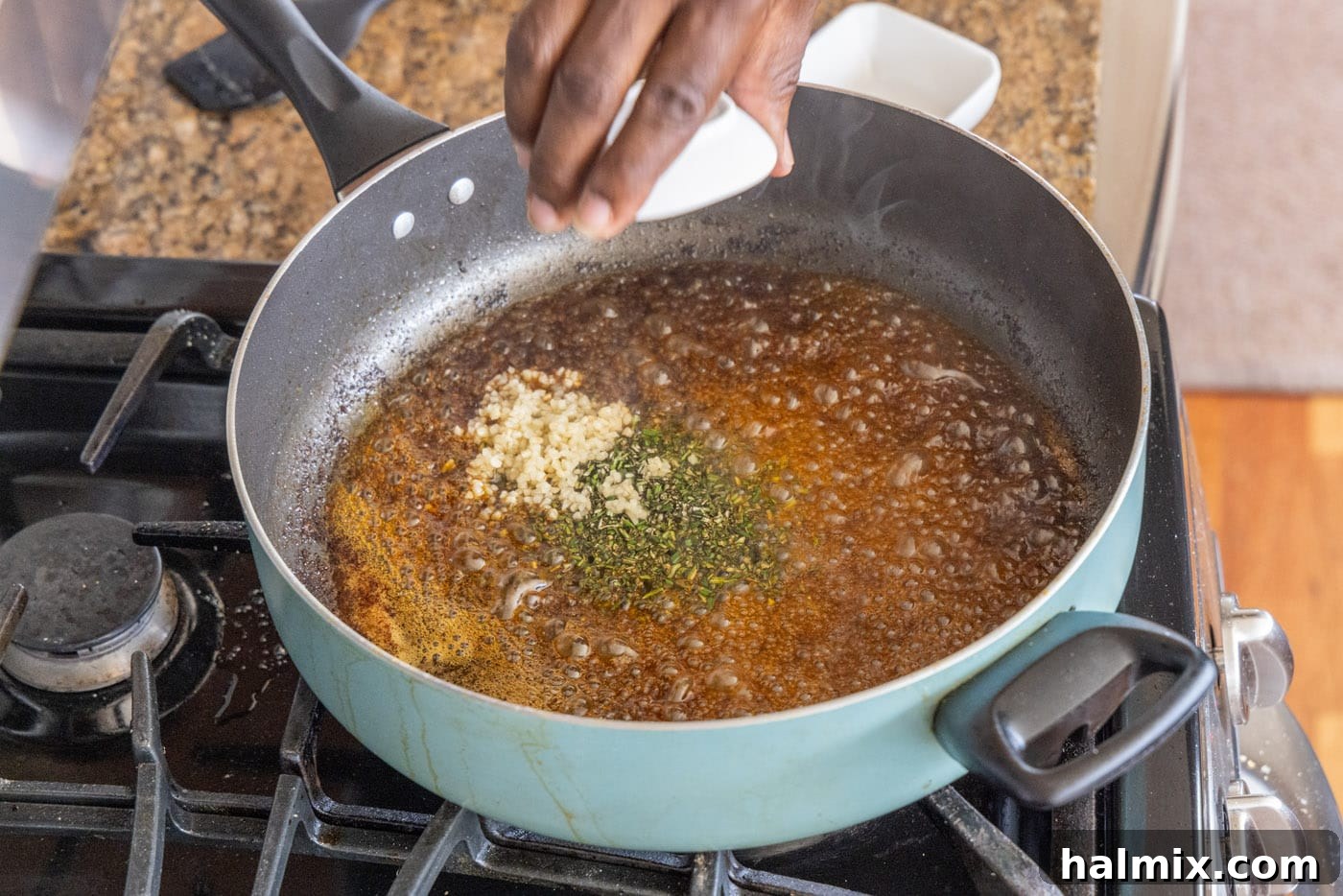 Adding minced garlic and fresh rosemary to the hot skillet, mixing with the pan drippings.
