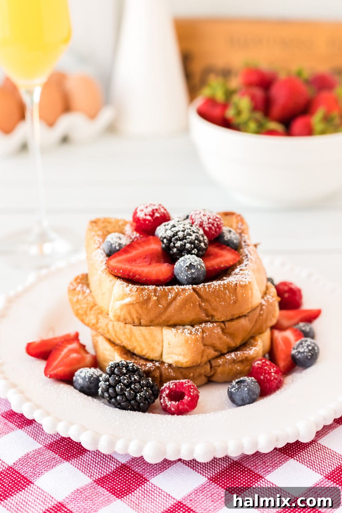 Plate of French Toast topped with fresh berries and powdered sugar, with a fork digging in.