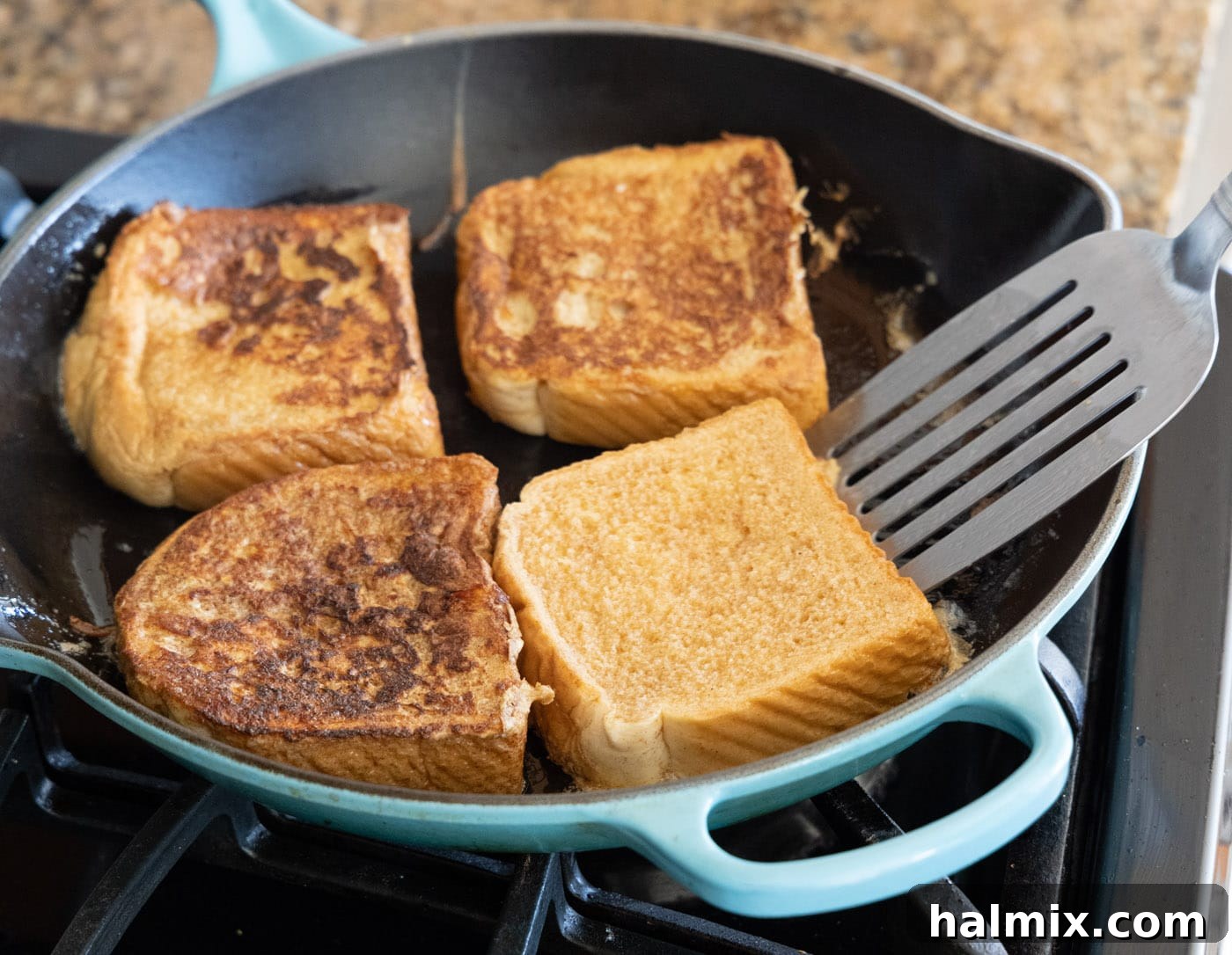 A spatula flipping a slice of French toast in a skillet, revealing a perfectly golden-brown underside.
