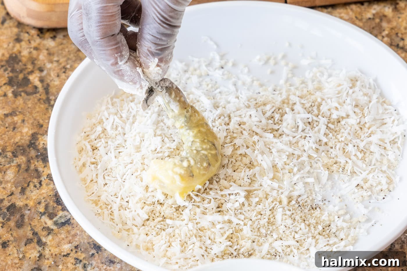 pressing flour and egg coated shrimp into coconut and breadcrumbs