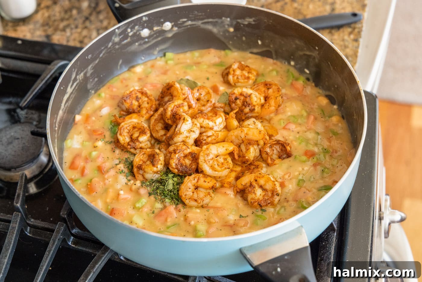 Cooked shrimp being added back into the rich etouffee gravy in a skillet.