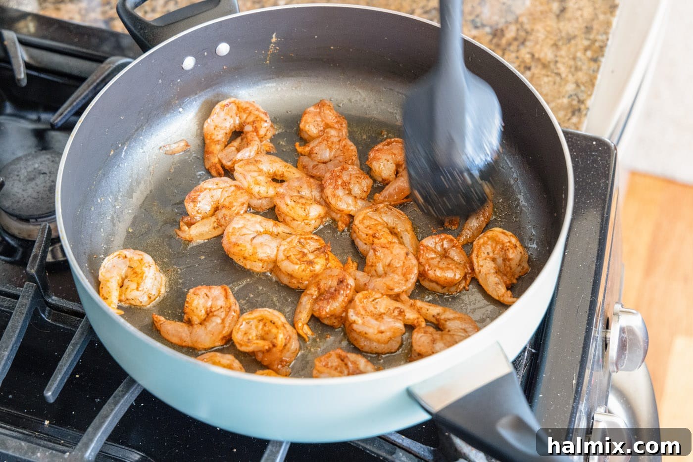 Shrimp lightly cooking in a hot skillet with olive oil, starting to turn pink.
