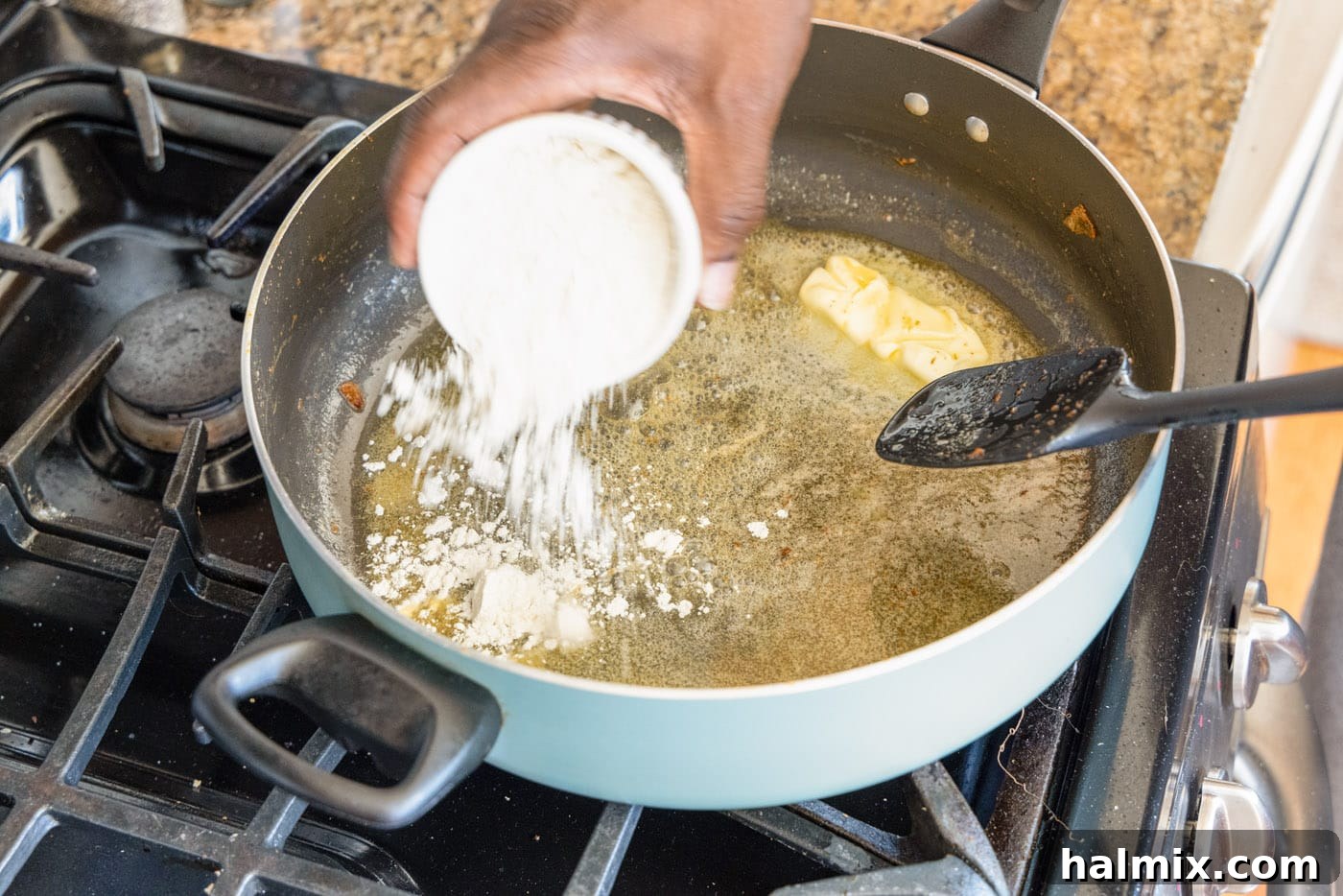 Flour being added to melted butter in a skillet to begin making a roux.
