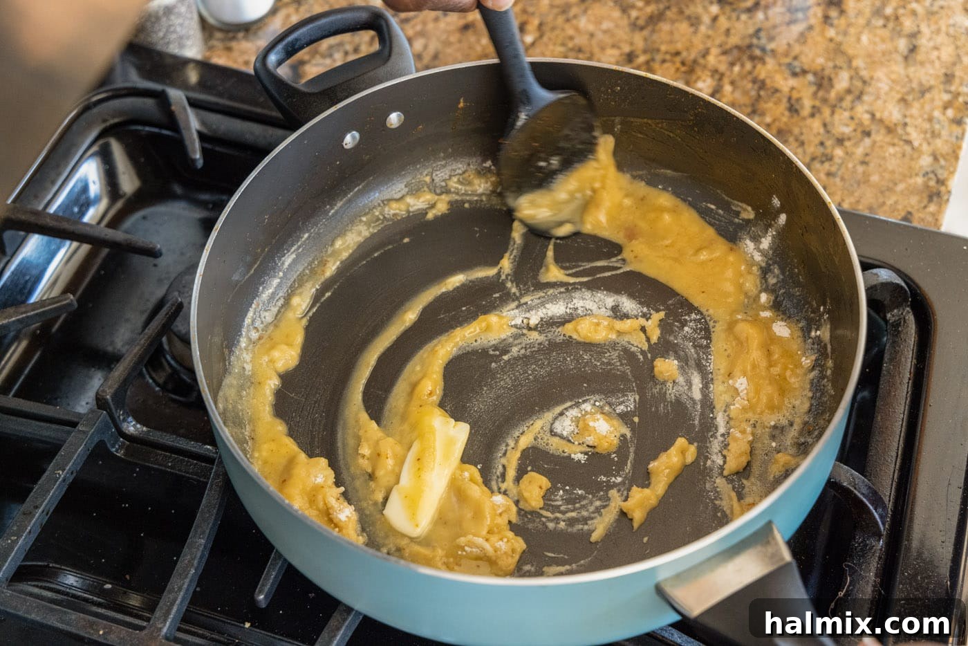 A spatula stirring the roux and added vegetables in a skillet, creating the base for the etouffee.