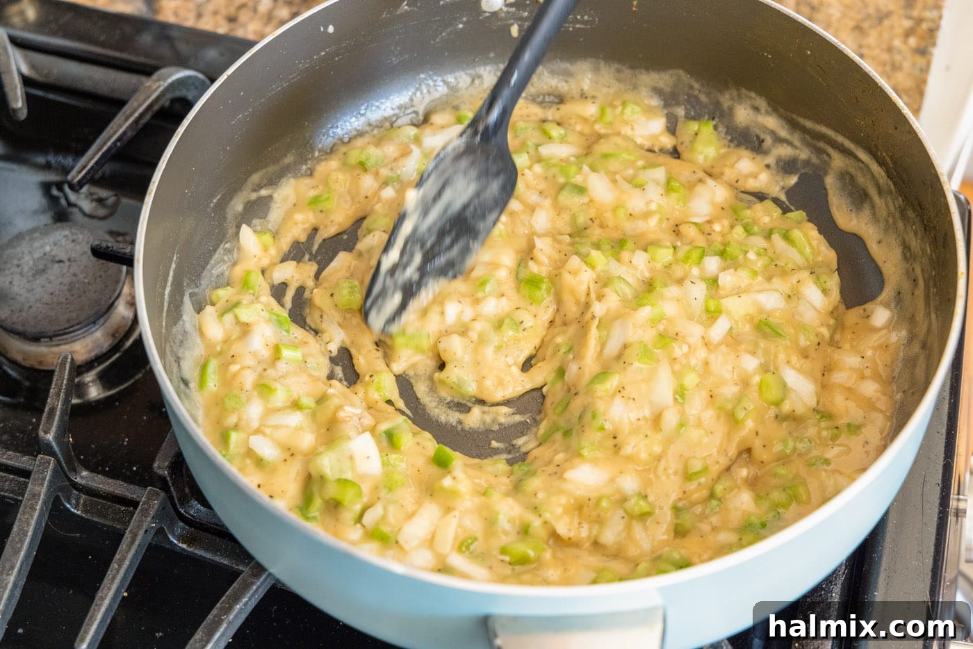 Various ingredients mixing into the roux and vegetables in a skillet to form the etouffee gravy.