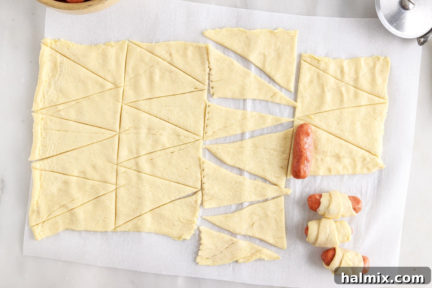 Sausage Swaddles 6 Placing a cocktail sausage on the wide end of a crescent dough triangle, ready to be rolled.