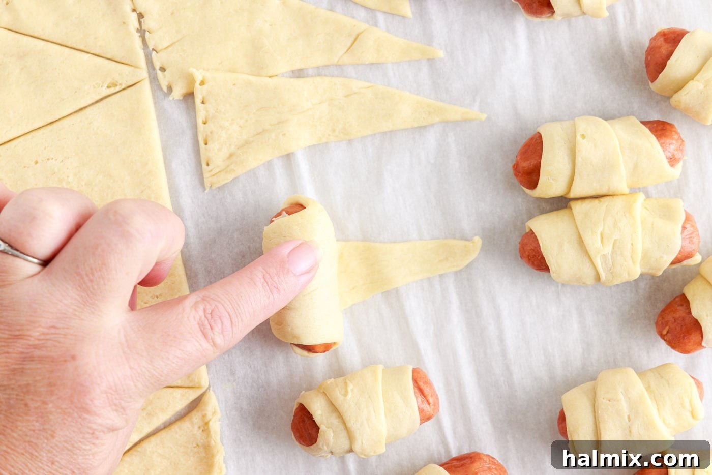 Sausage Swaddles 7 Rolling a mini sausage into crescent dough, demonstrating the wrapping technique.