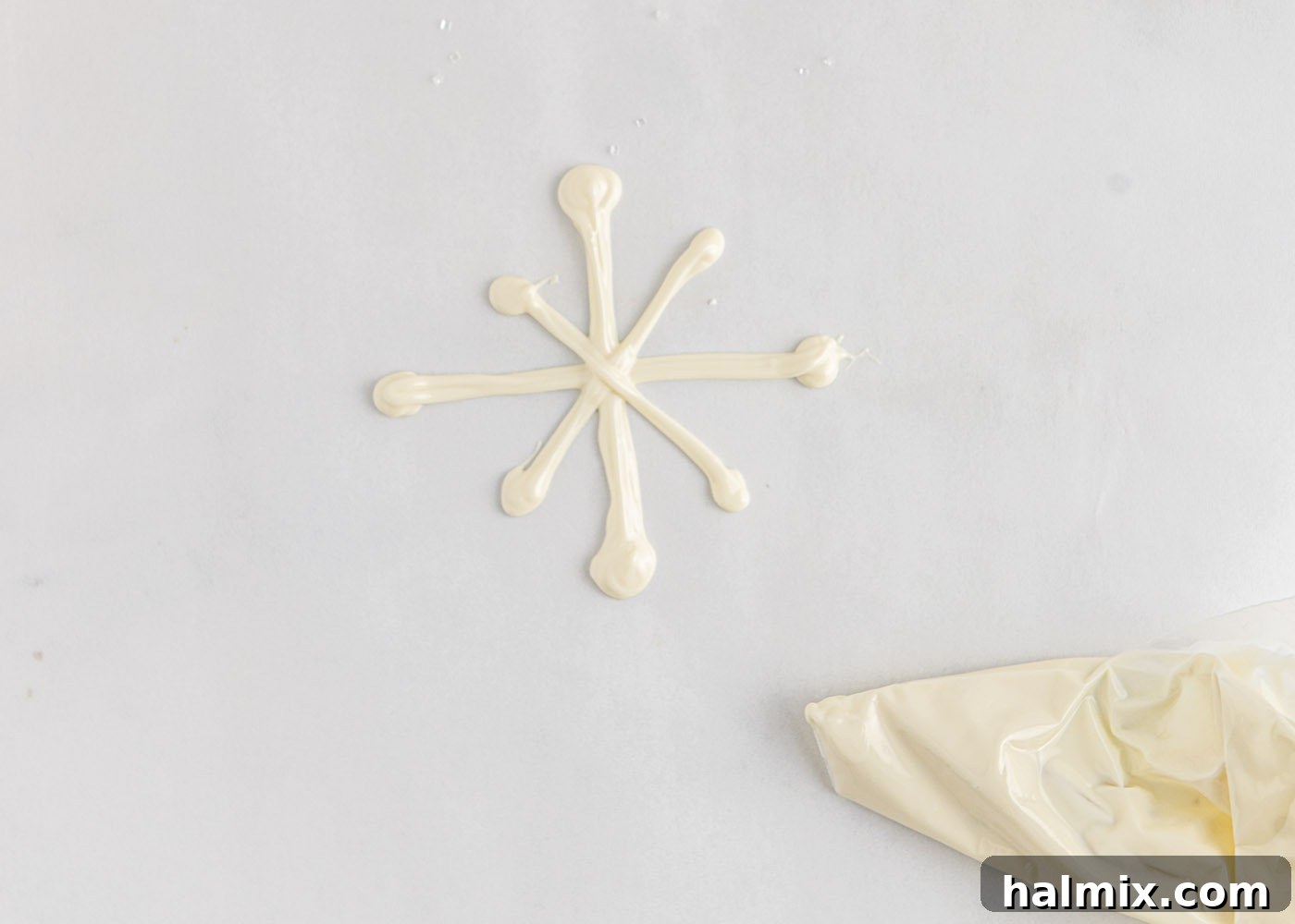 Piping a white chocolate snowflake design onto parchment paper