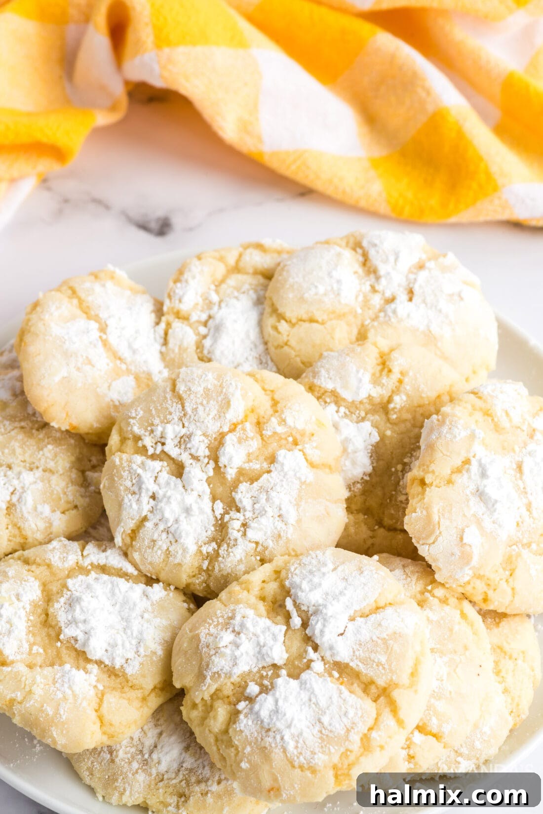 Soft and chewy Orange Crinkle Cookies, made with real orange juice and zest, rolled in powdered sugar for a beautiful crinkled finish. A close-up of freshly baked orange crinkle cookies on a white plate, showcasing their characteristic powdered sugar coating and delicate cracked surface, ready to be enjoyed.