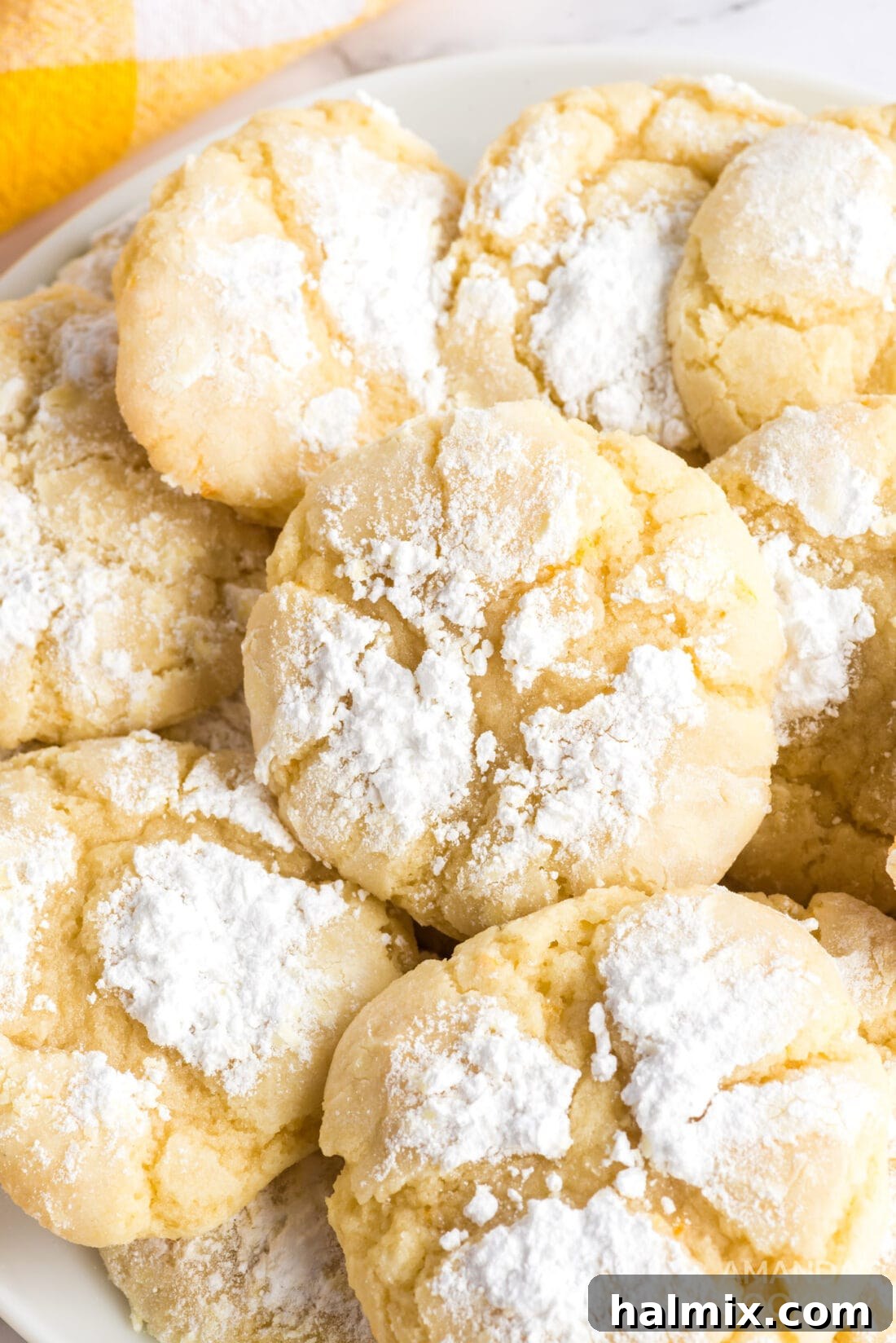 Orange Crinkle Cookies are soft, chewy cookies bursting with real orange flavor, rolled in powdered sugar for a beautiful and delicious finish. A close-up shot of several orange crinkle cookies, perfectly baked with a soft, cracked texture and a generous dusting of powdered sugar, presented on a light-colored plate.