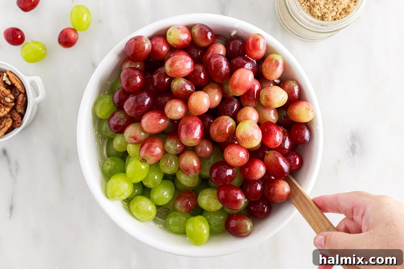 red and green grapes being added to a large bowl of creamy dressing
