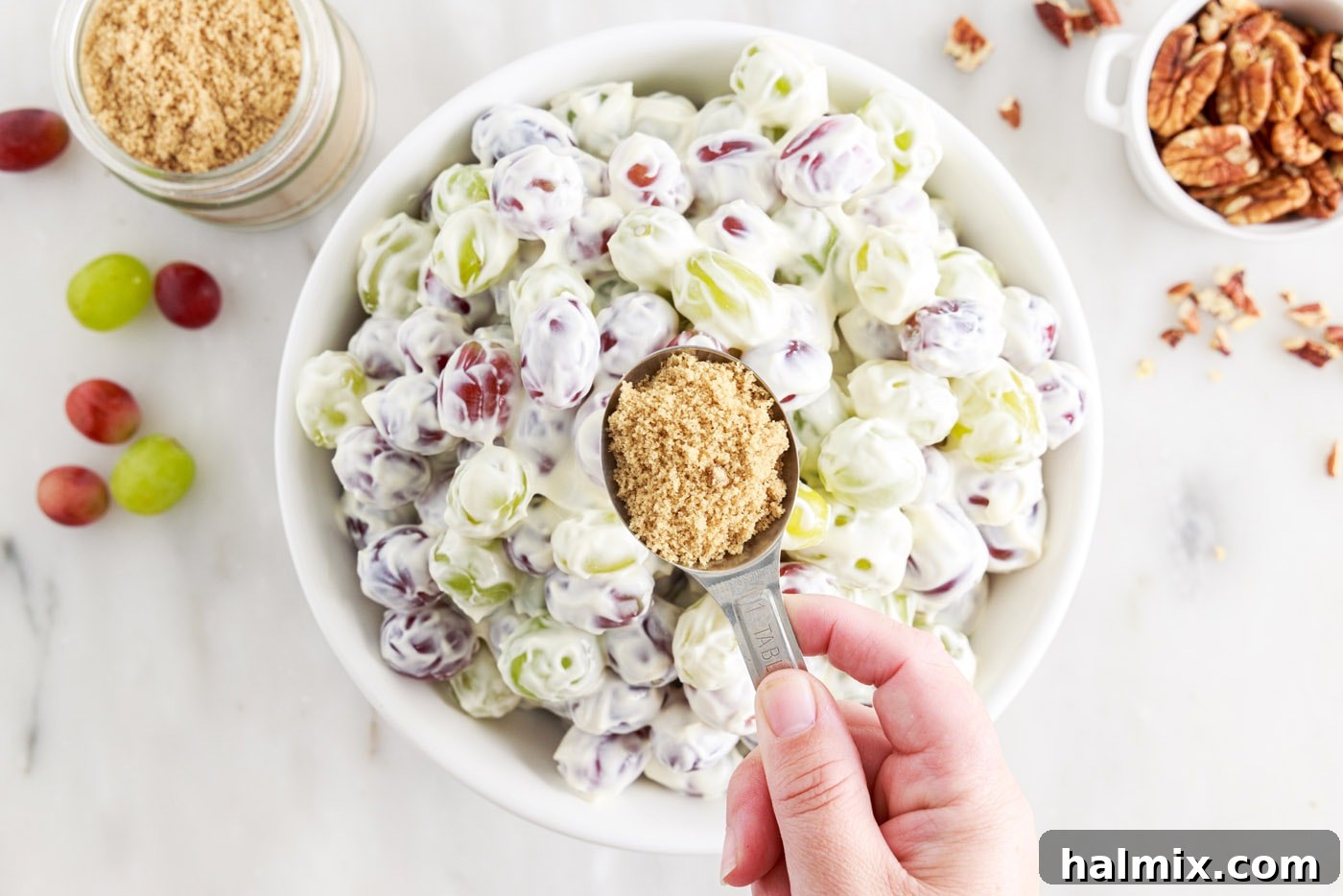 hand sprinkling brown sugar over a bowl of grape salad