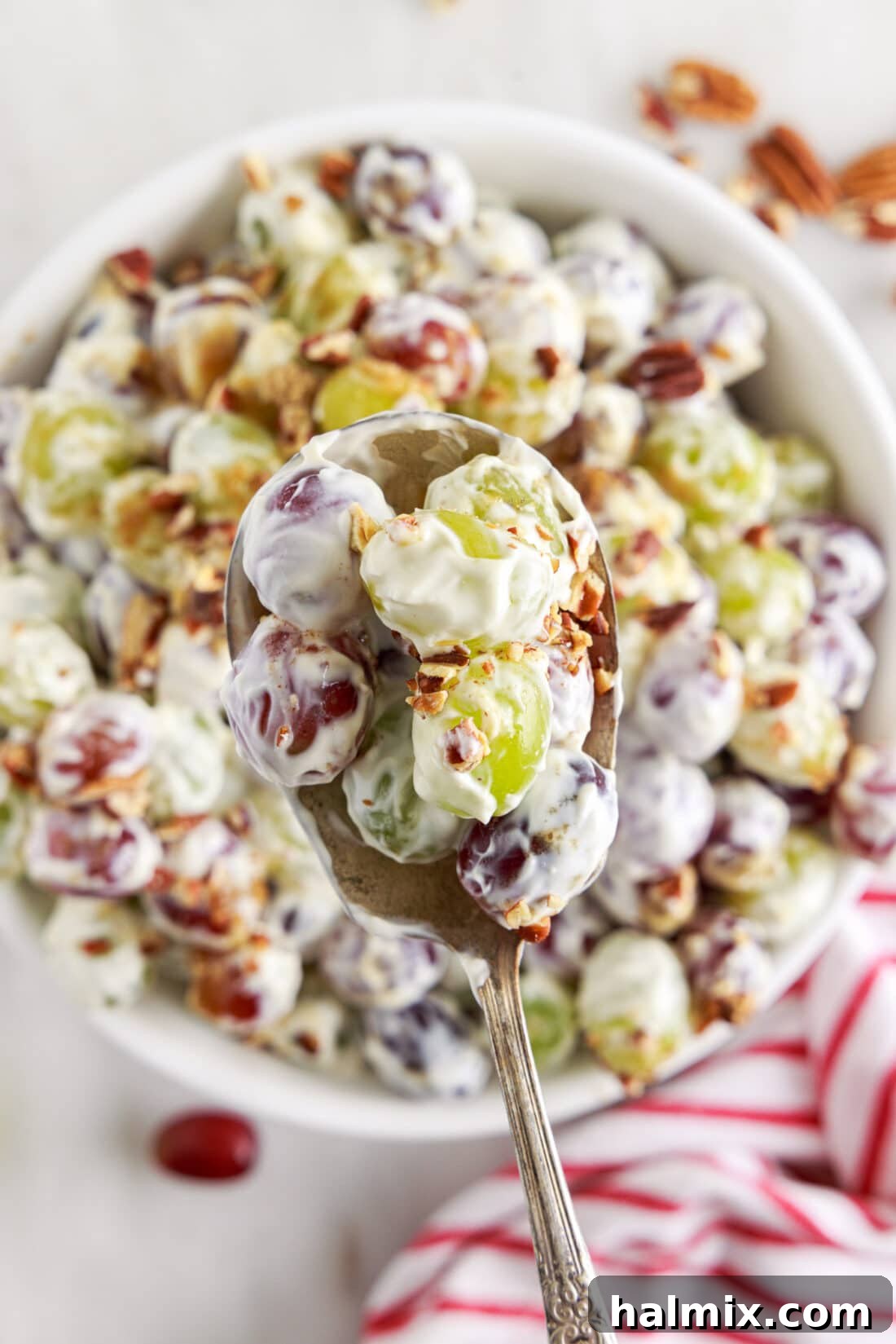 spoon of Grape Salad above a serving bowl, showcasing the creamy texture and pecan topping
