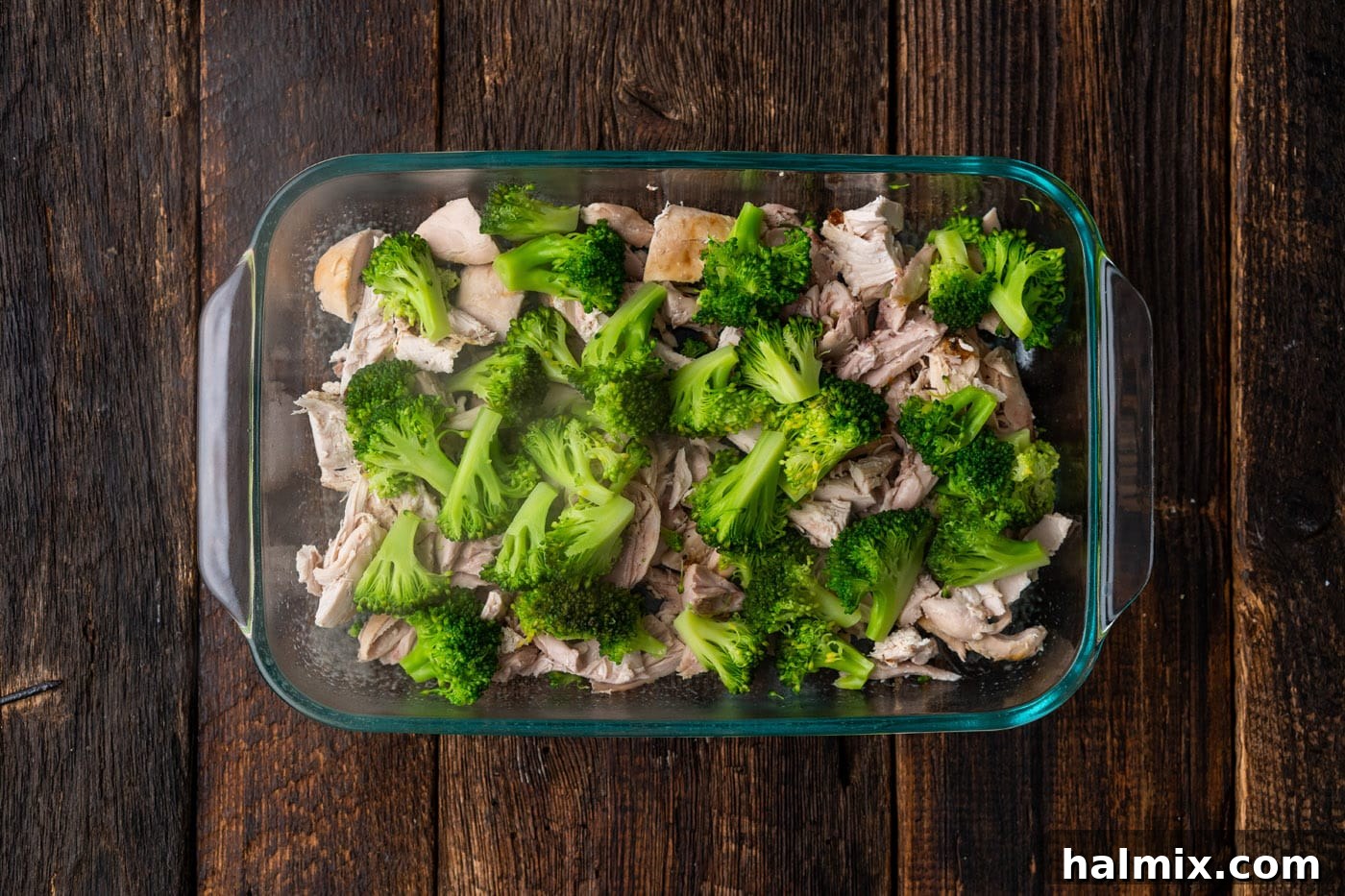 Broccoli florets spread over the layer of chicken in the casserole dish.
