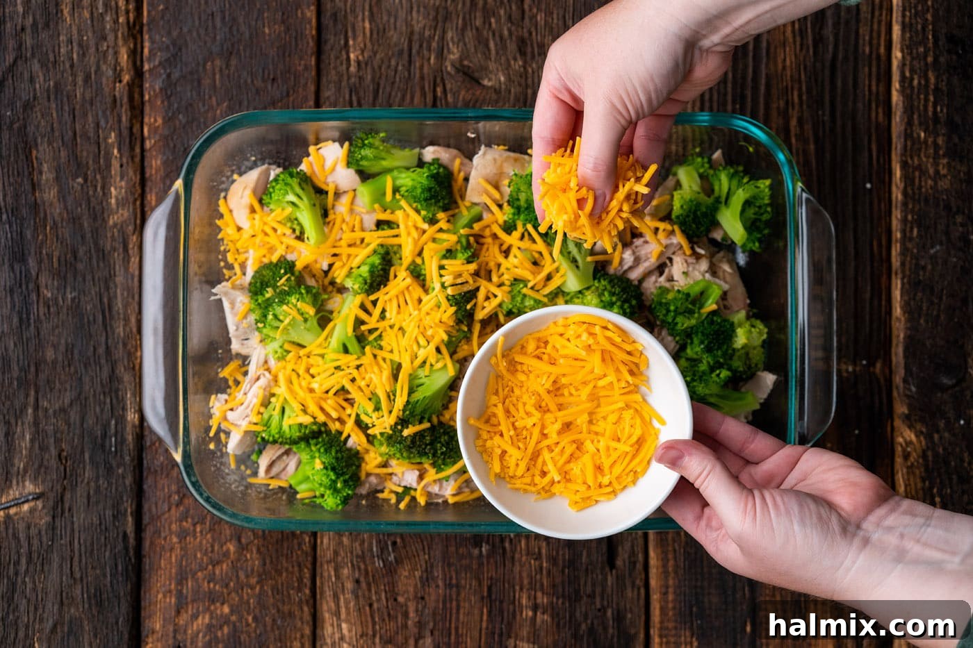 Shredded cheddar cheese being sprinkled generously over the broccoli and chicken.