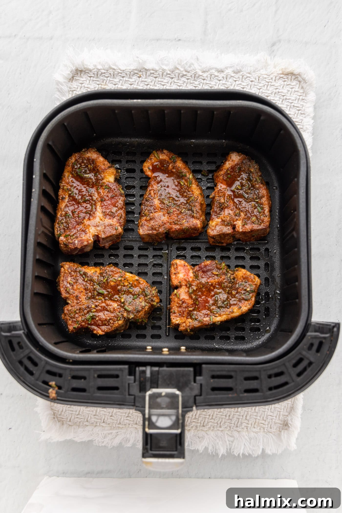 Raw, marinated lamb chops placed neatly in a single layer within the air fryer basket