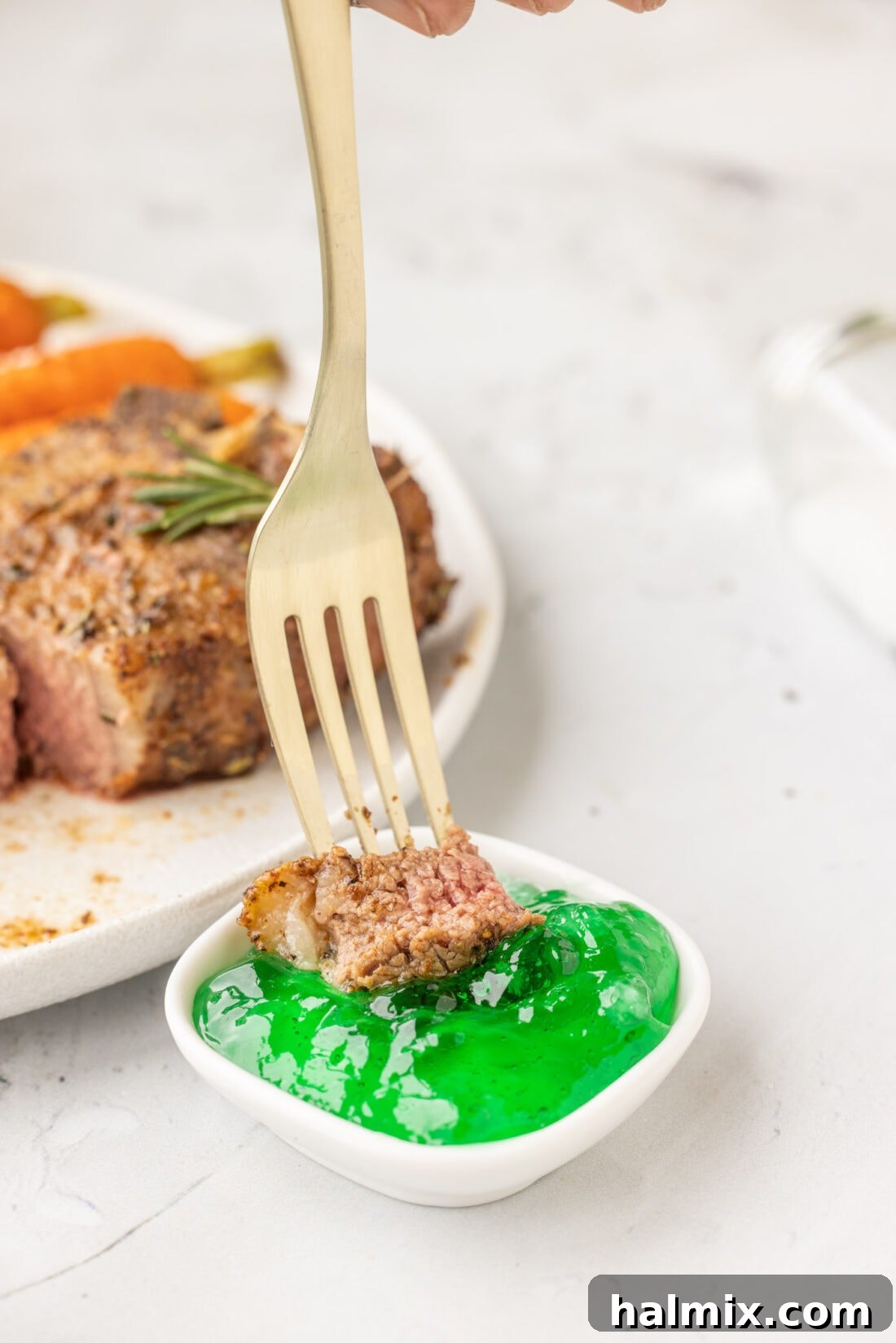 A hand dipping a perfectly cooked Air Fryer Lamb Chop into a small bowl of vibrant green mint jelly