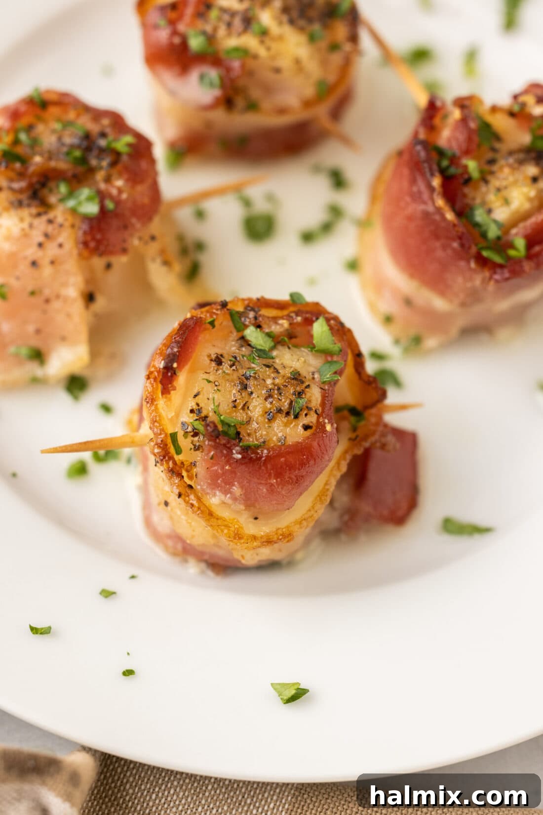 Perfectly cooked bacon wrapped scallops served on a white plate, garnished with fresh herbs, ready to be enjoyed.