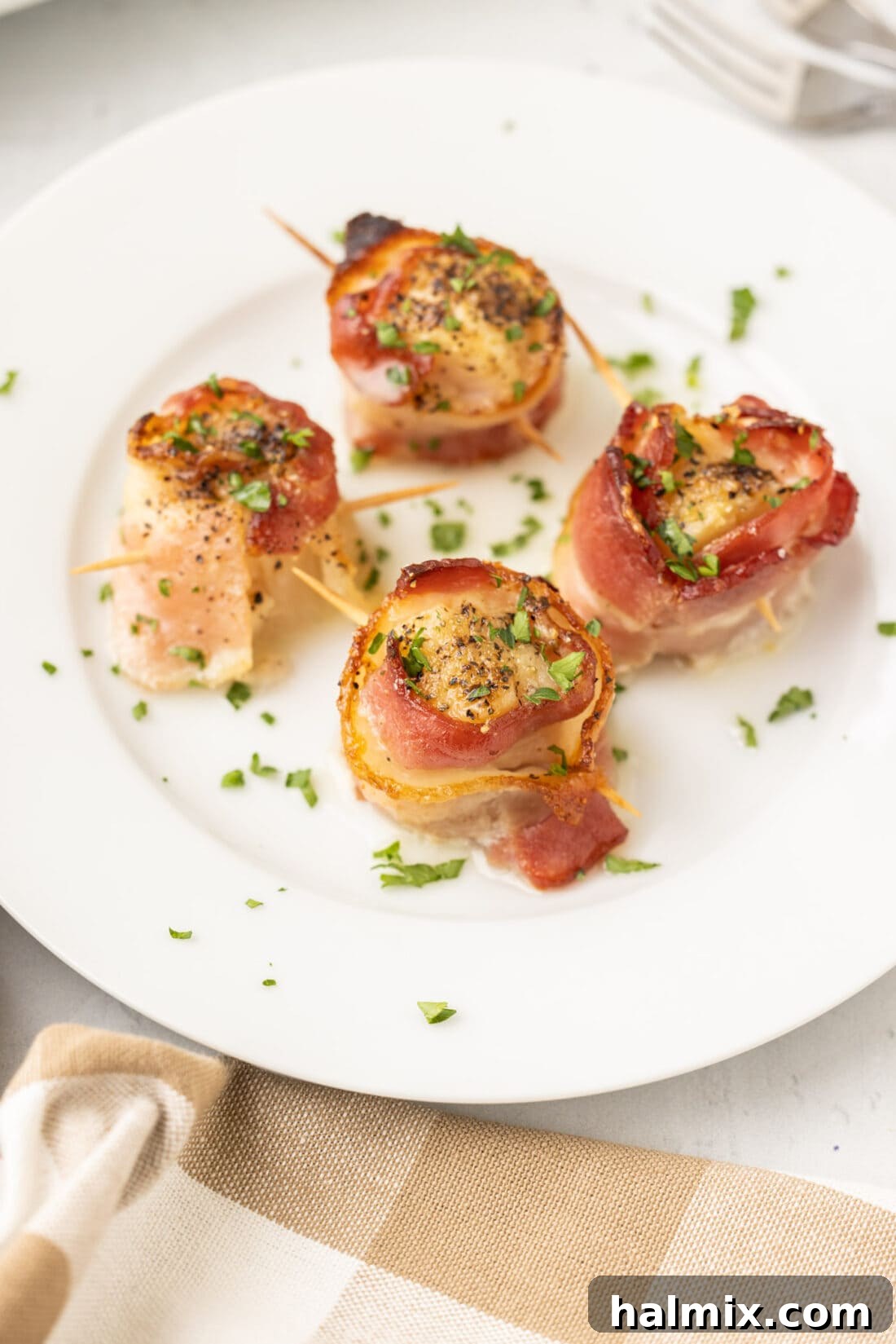 A beautifully arranged plate of bacon wrapped scallops, golden and crispy, garnished with fresh greens, ready to be served.