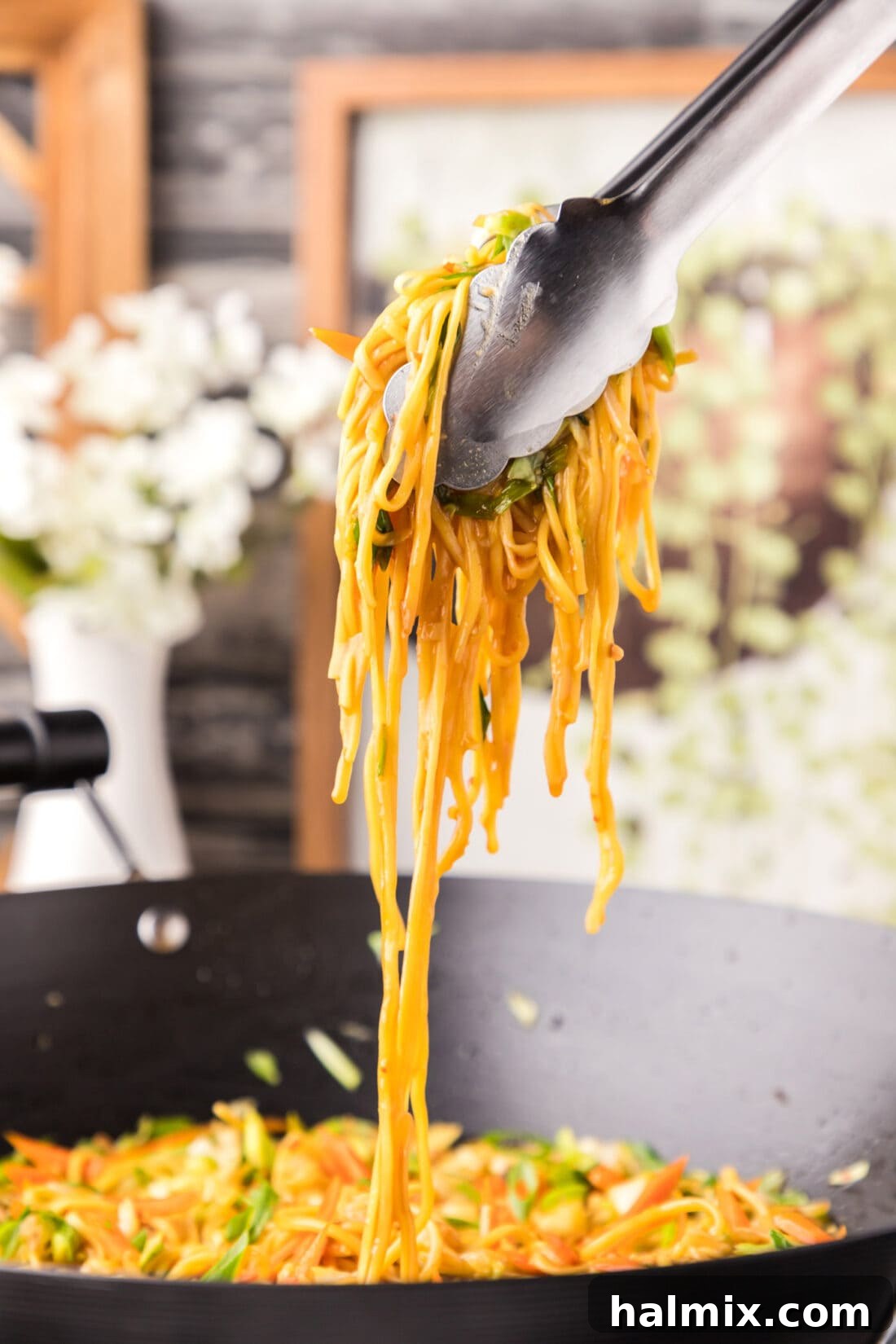 Tongs lifting delicious homemade Chow Mein from a serving bowl, showcasing the vibrant noodles and vegetables.