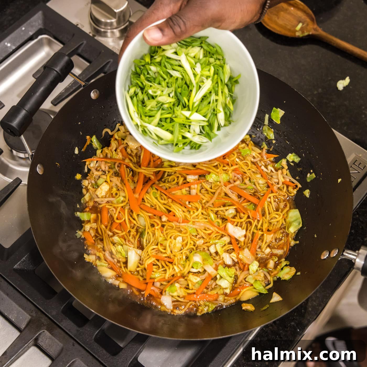 Adding green onions to skillet of chow mein