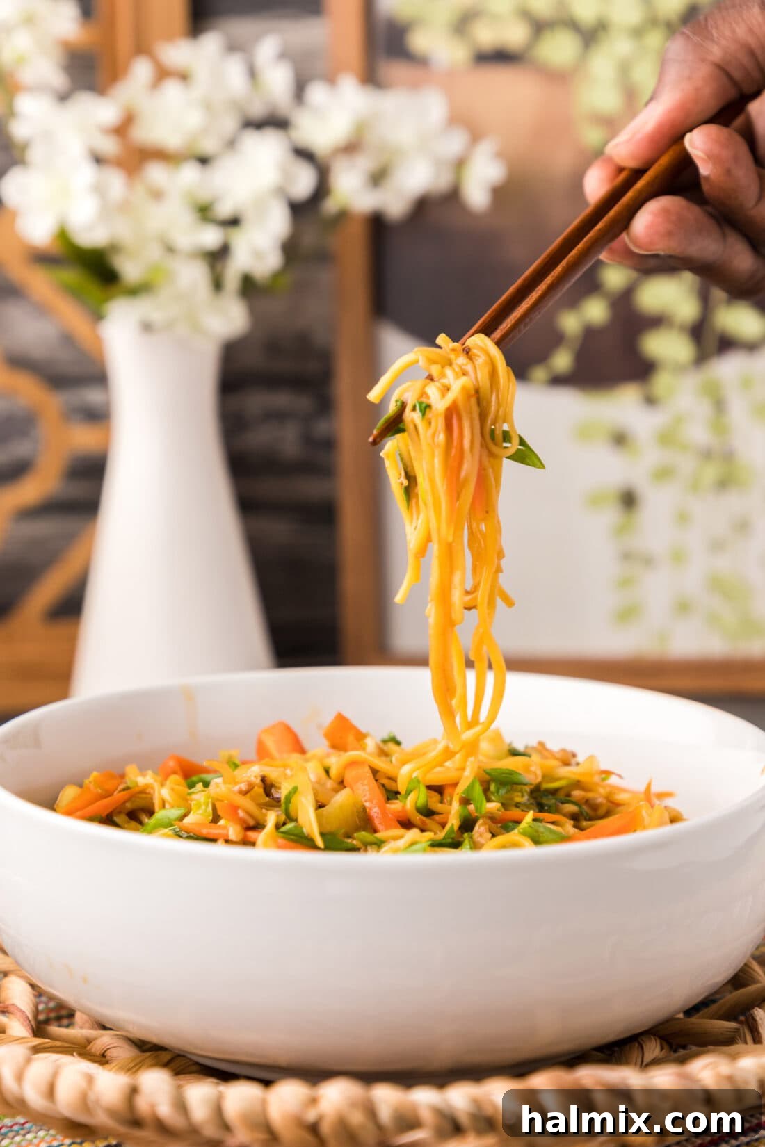 A close-up of Chow Mein being lifted with chopsticks, showing the texture and ingredients.