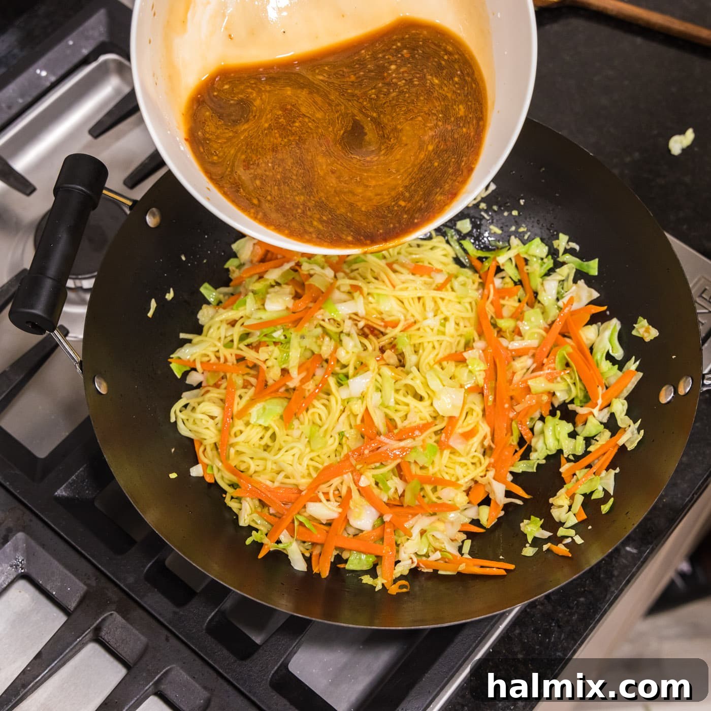 Pouring chow mein sauce into wok with vegetables