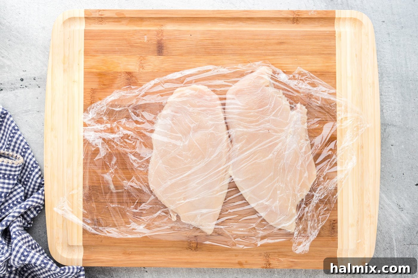 Pounding Chicken Breasts Evenly Chicken breasts covered with plastic wrap being pounded to an even thickness