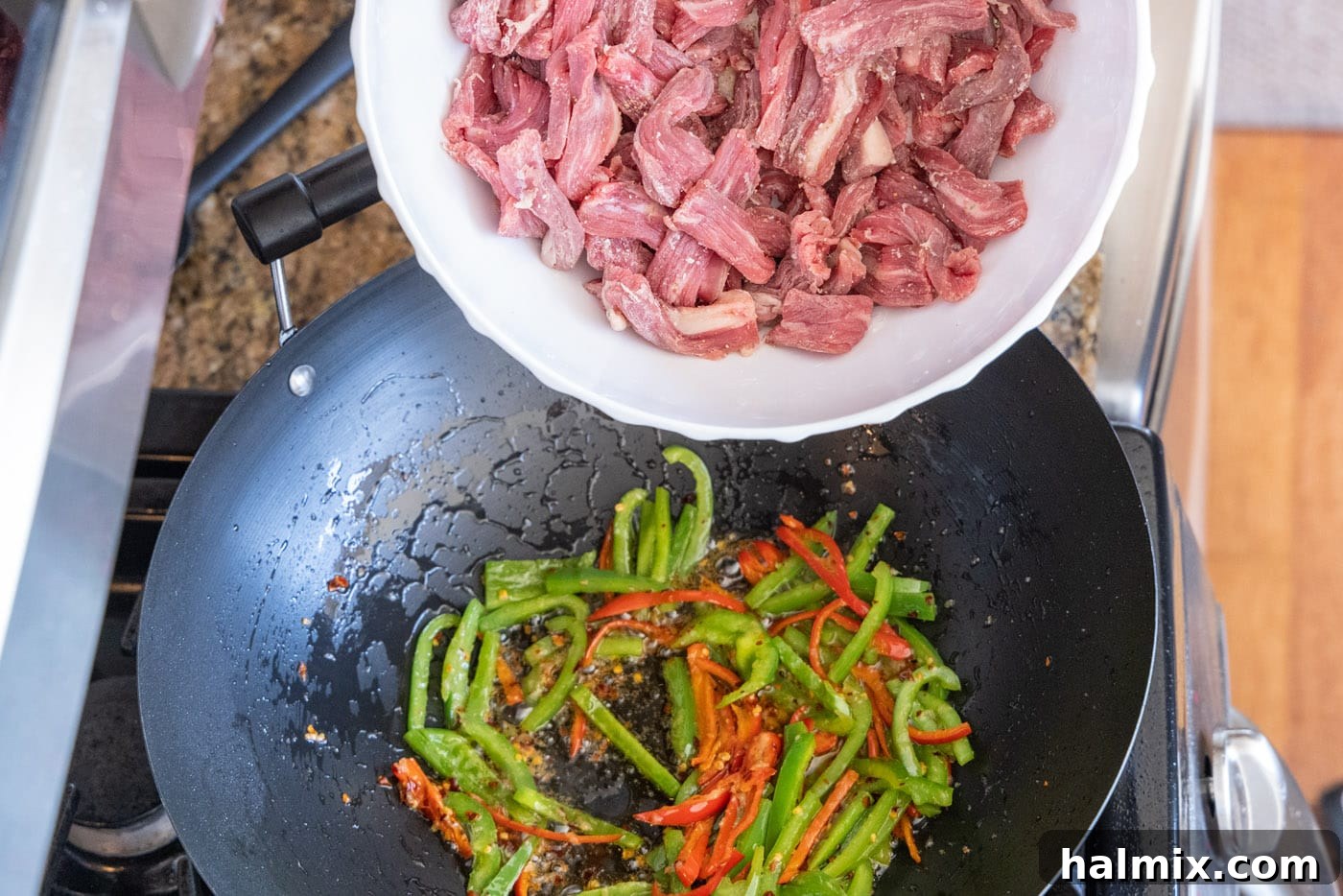 Adding seasoned flank steak to the stir-frying vegetables in the wok