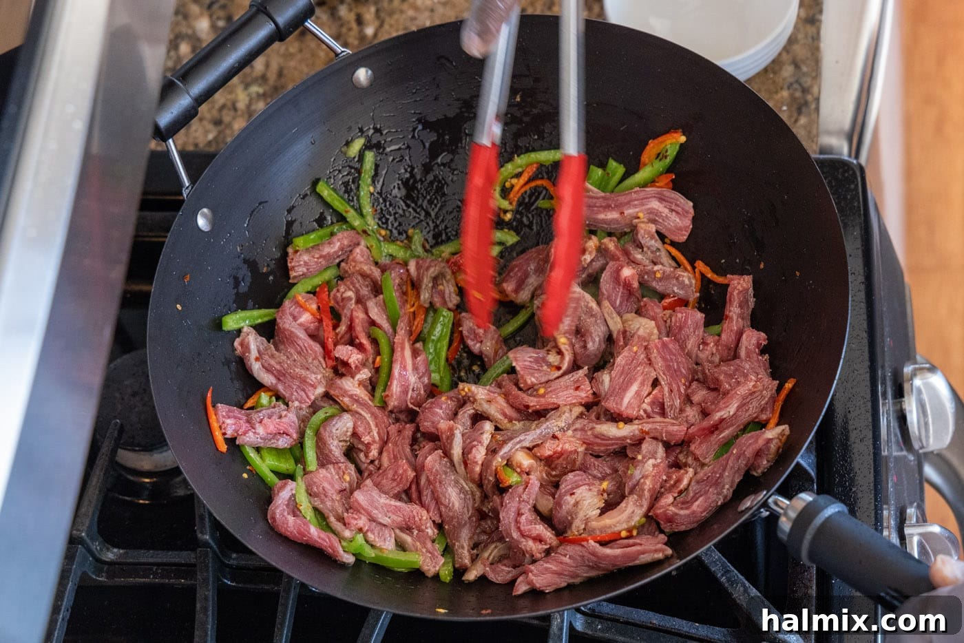 Mixing beef and veggies in wok, ensuring everything cooks evenly