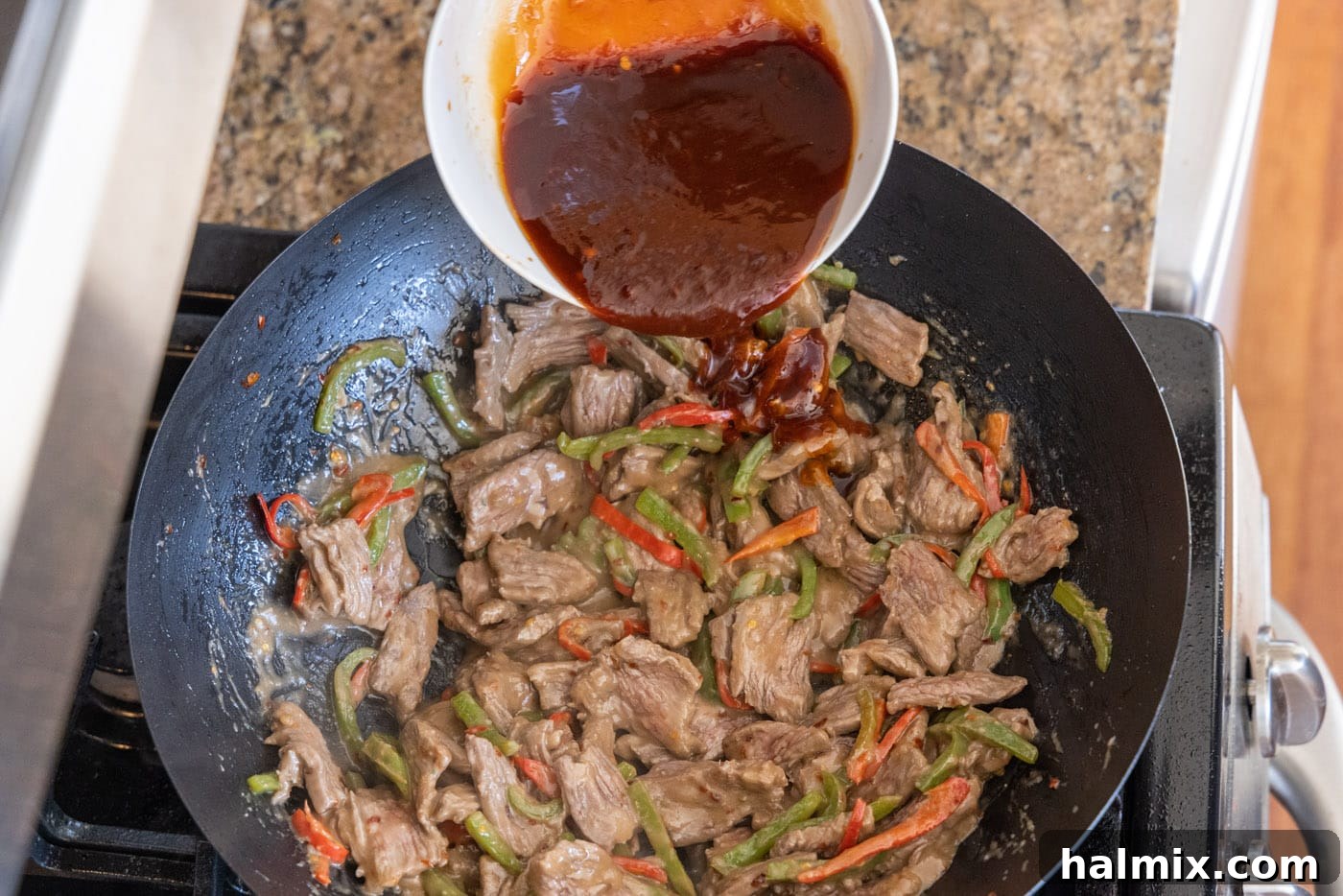 Pouring the rich Kung Pao sauce over the beef and vegetables in the wok