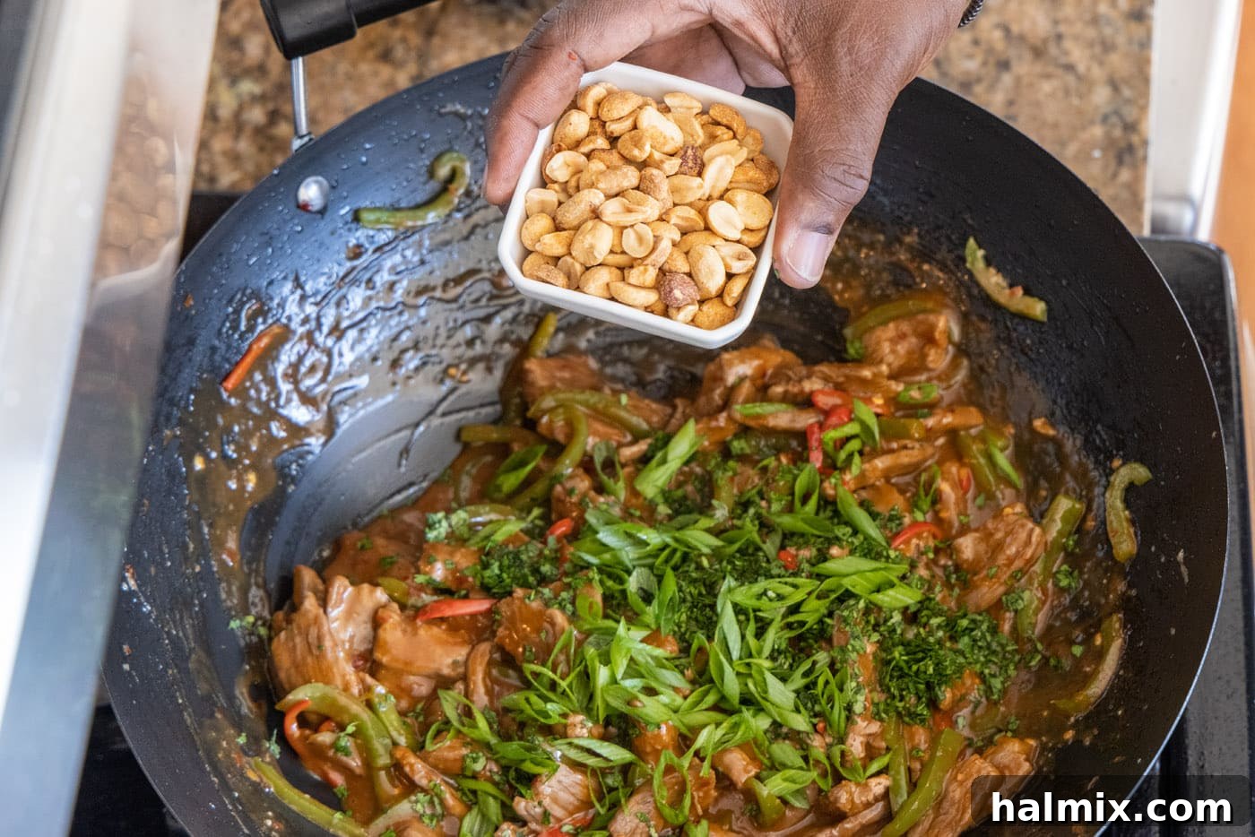 Roasted peanuts, cilantro, and green onions being added to the finished Kung Pao Beef