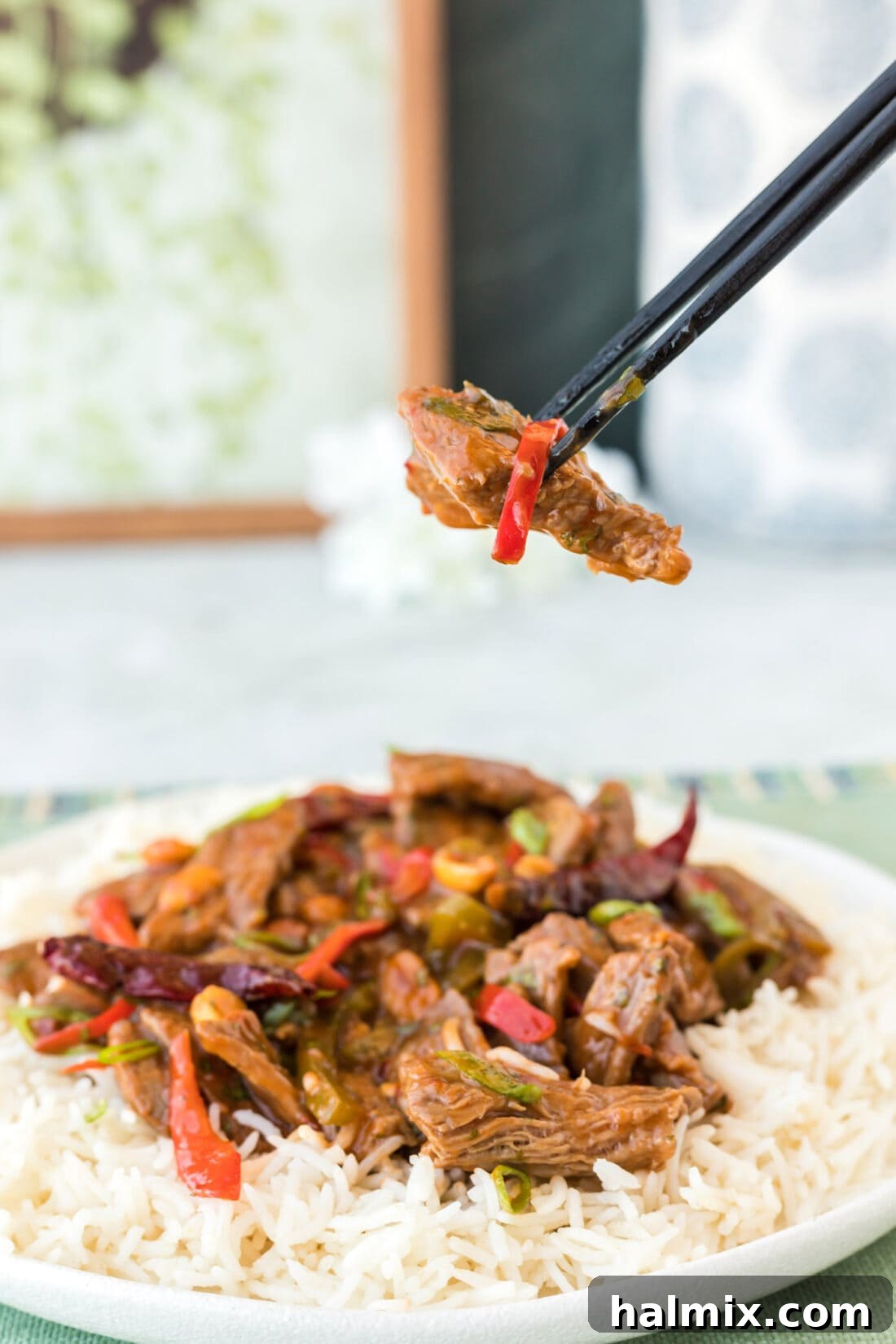 Chopsticks lifting a piece of tender Kung Pao Beef from a wok, highlighting the perfect stir-fry texture