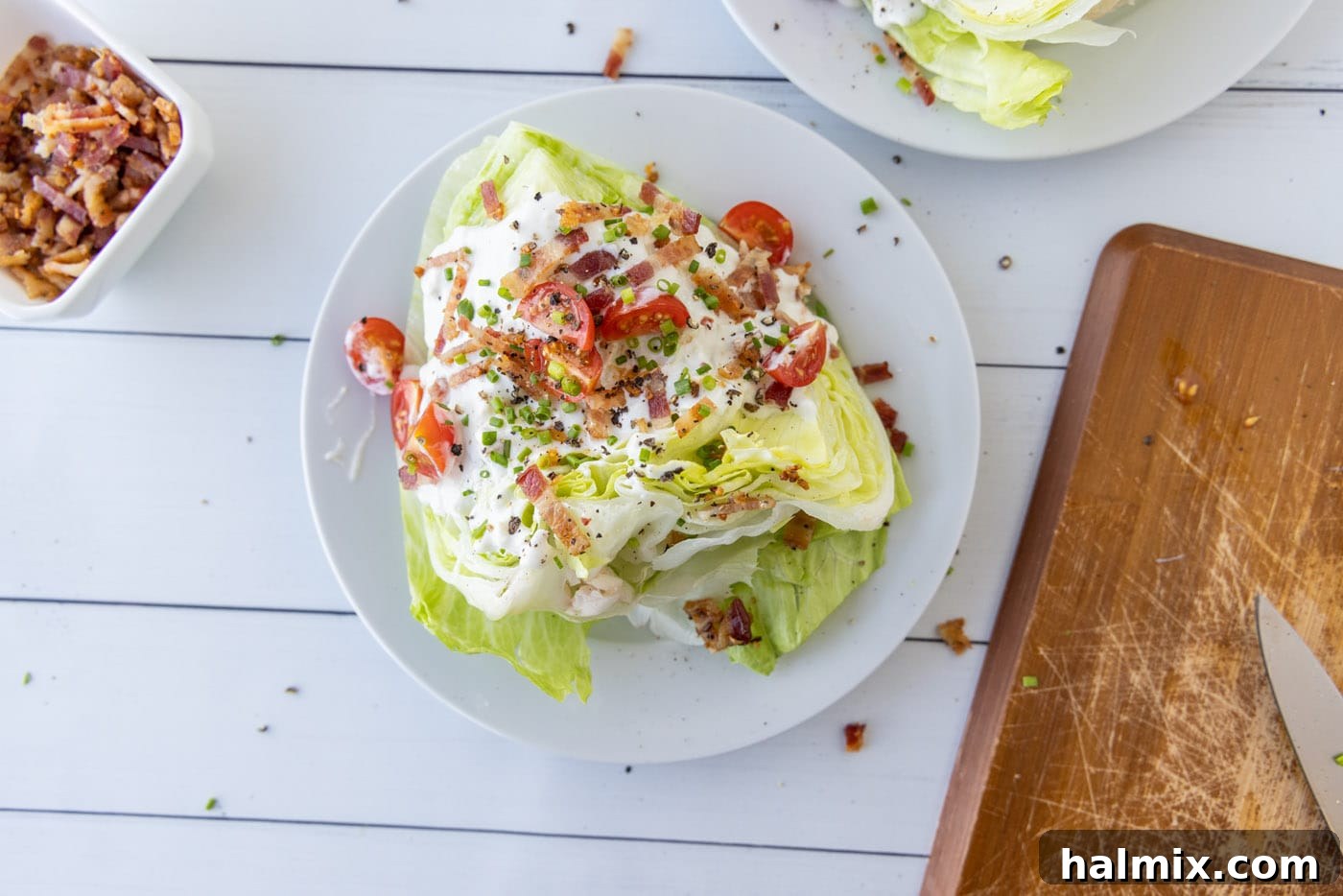 Chives and bleu cheese crumbles are added to a wedge salad with bacon and dressing.
