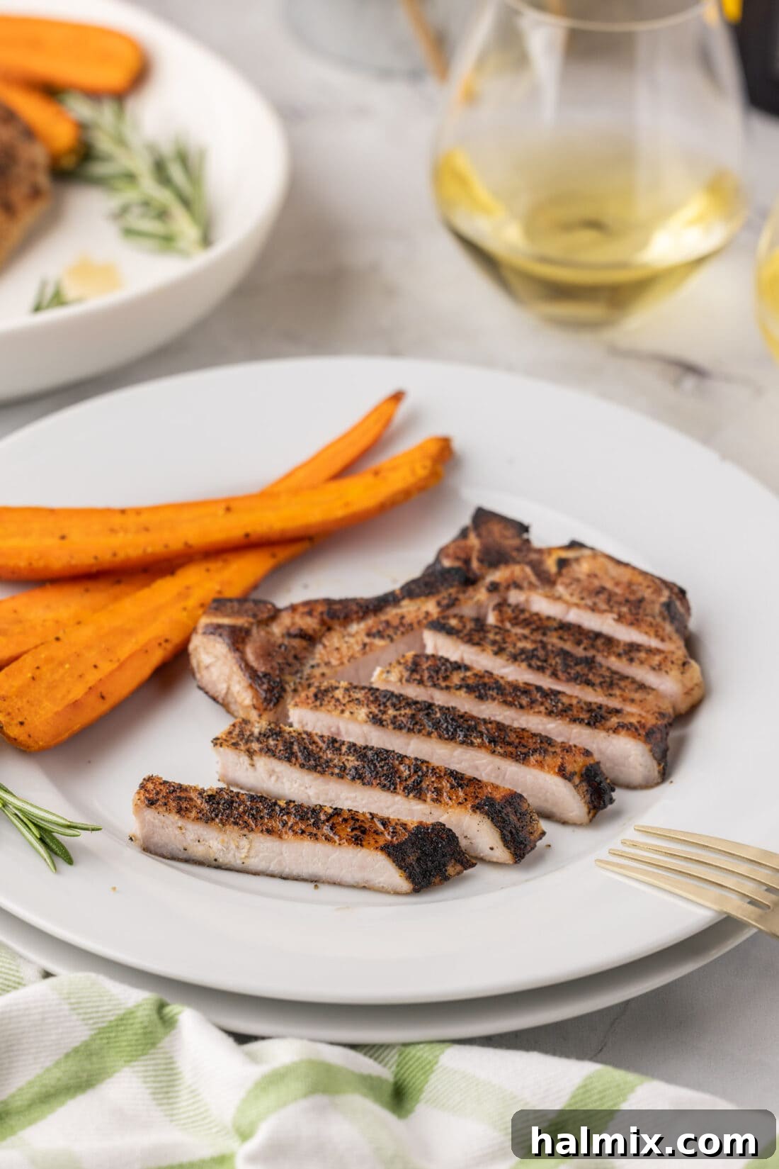 Plate of perfectly sliced Sous Vide Pork Chop revealing its juicy, medium-done interior, garnished with herbs.