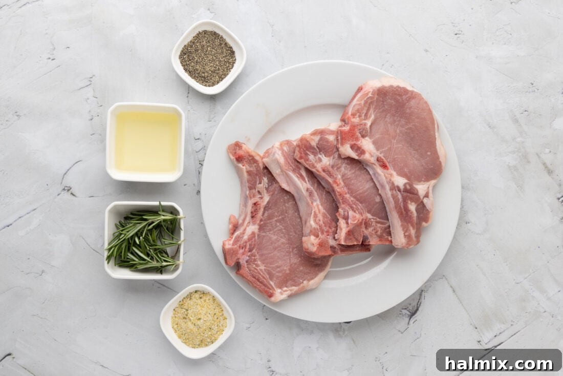 Ingredients laid out for Sous Vide Pork Chops: raw pork chops, olive oil, garlic salt, black pepper, and fresh rosemary sprigs.