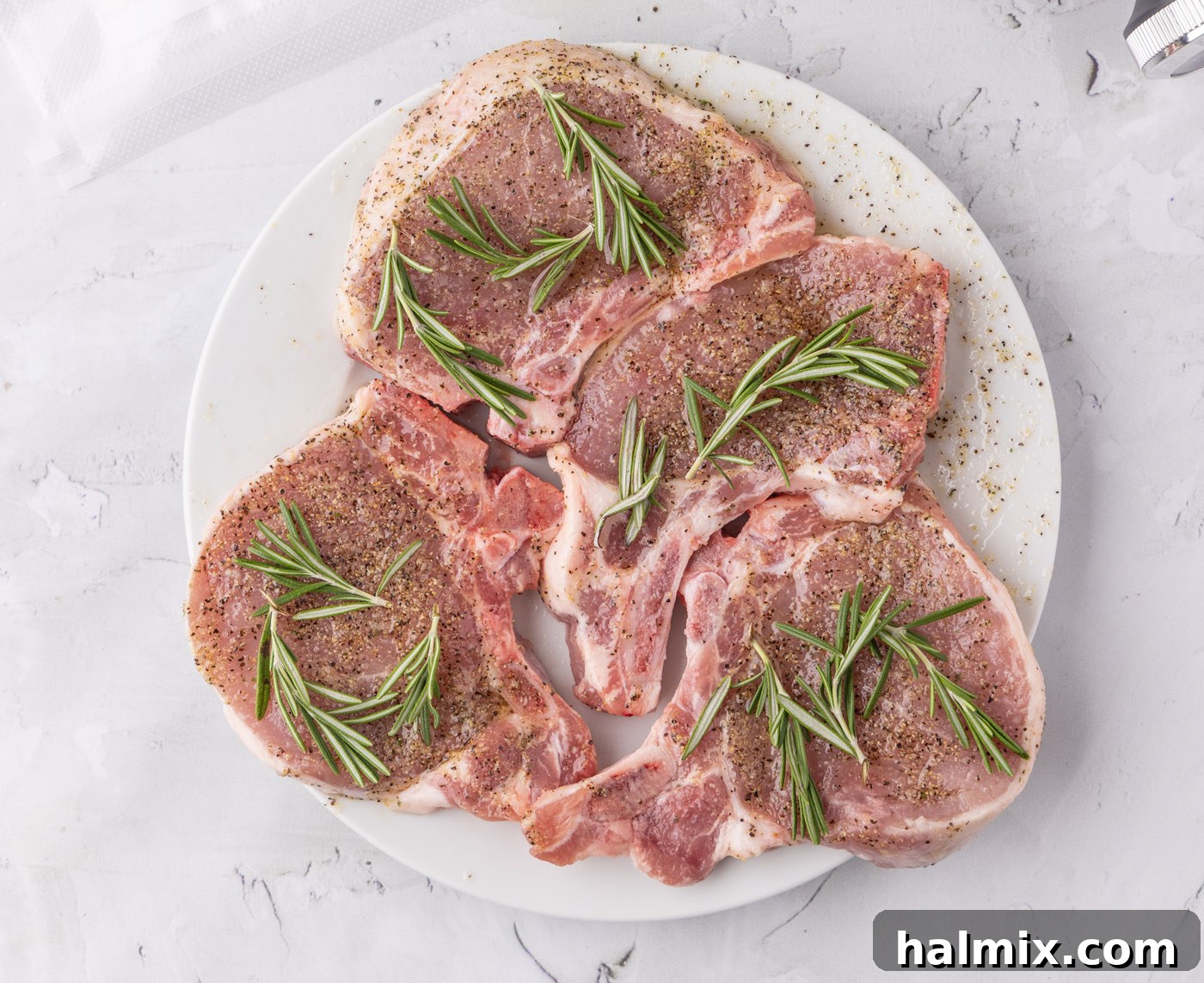 Pork chops coated in a wet rub and topped with fresh rosemary sprigs, ready for vacuum sealing.