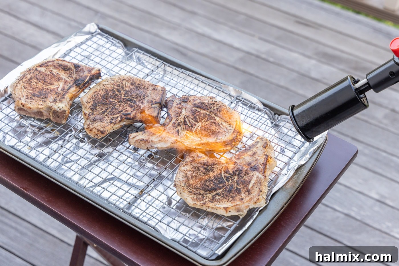 Kitchen torch expertly searing the exterior of a cooked sous vide pork chop for a beautiful crust.