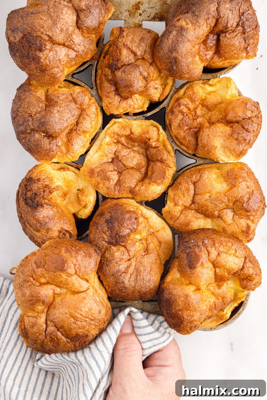 Golden Popovers 3 A hand lifting a hot popover pan filled with perfectly risen, golden-brown popovers from the oven.