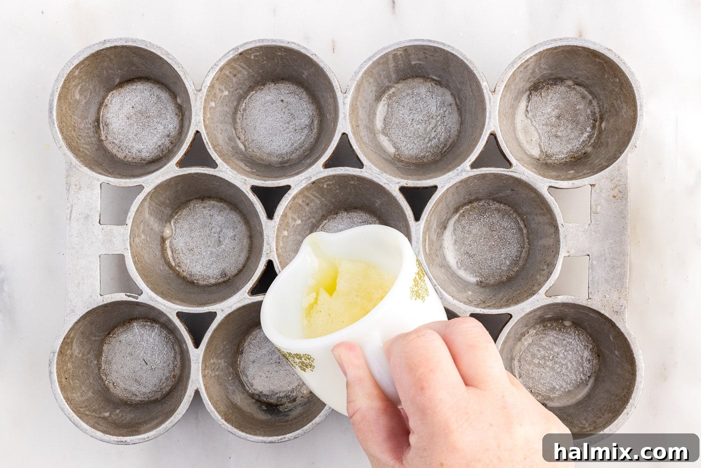 Golden Popovers 8 Carefully pouring melted butter into the hot cups of a popover pan, preparing them for batter.