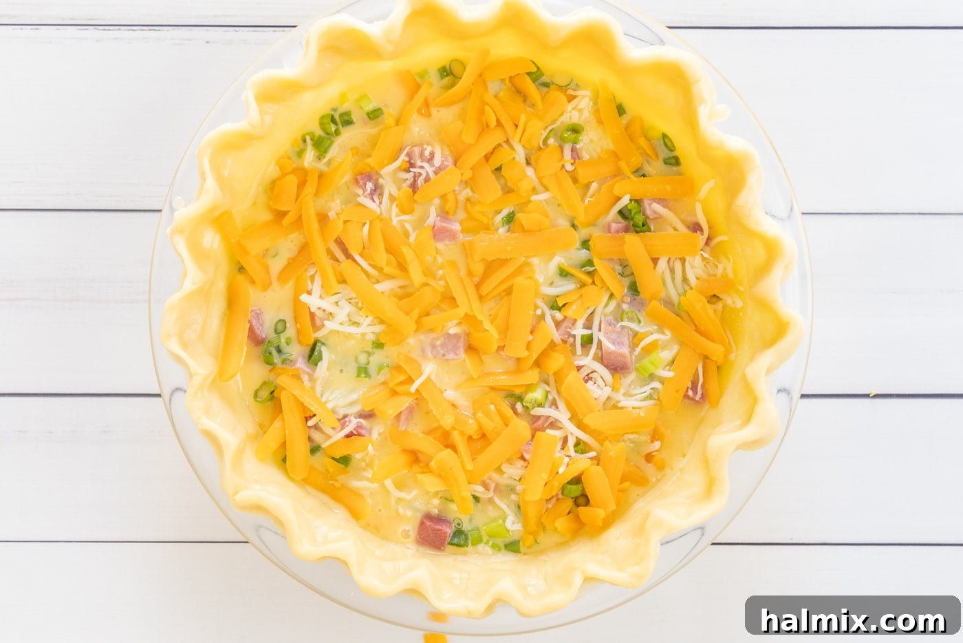 A generous topping of cheddar and mozzarella cheese on the quiche before baking.