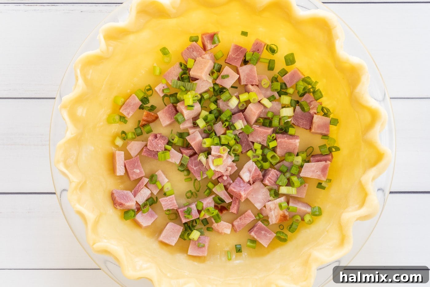 Cubed ham and sliced green onions placed evenly in a pie shell.