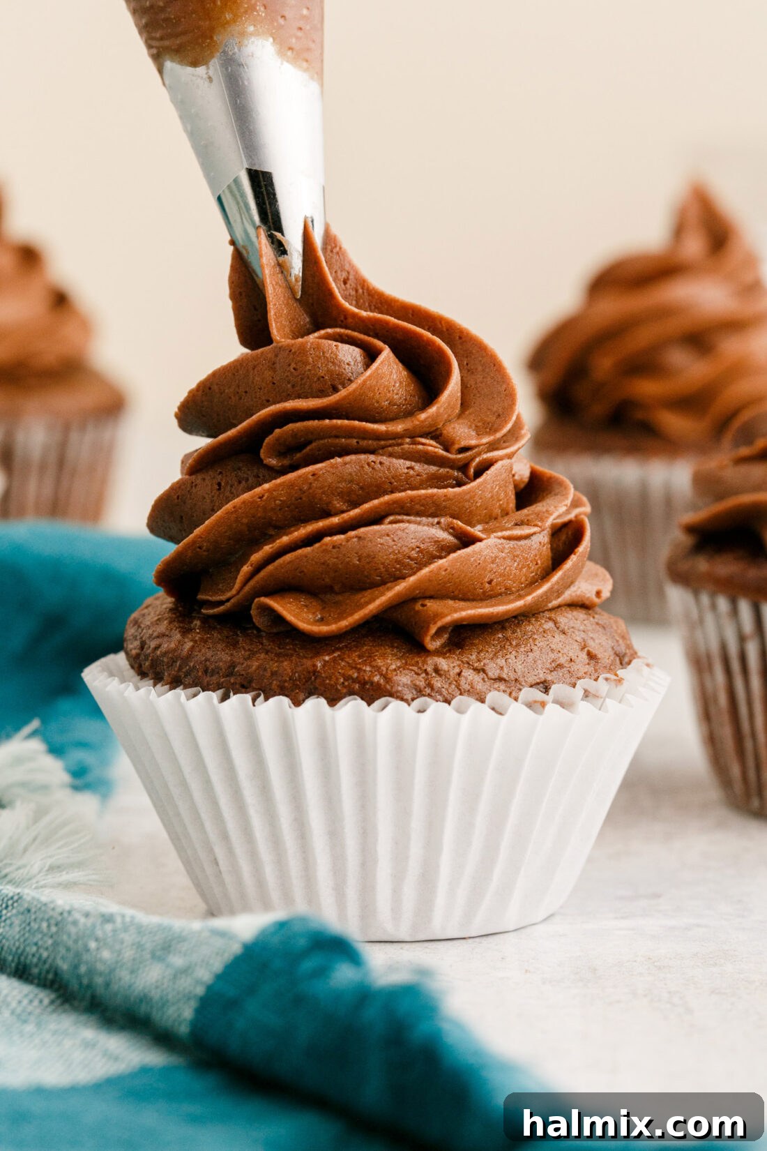 piping rich, dark chocolate buttercream frosting onto a freshly baked cupcake with a decorative tip