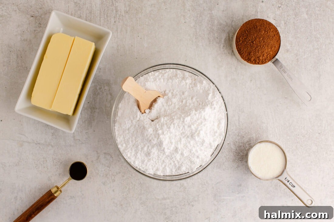all five ingredients for chocolate buttercream frosting laid out on a surface: butter, powdered sugar, cocoa powder, vanilla extract, heavy cream