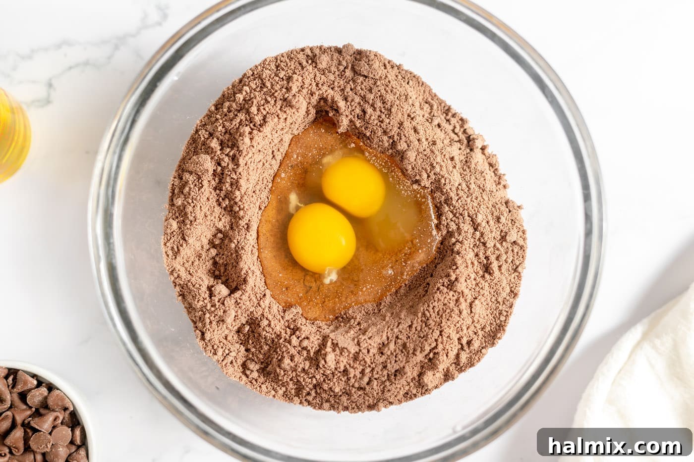 Luscious Chocolate Cake Mix Bites 5 Eggs cracked into a well in the center of chocolate cake mix in a bowl.