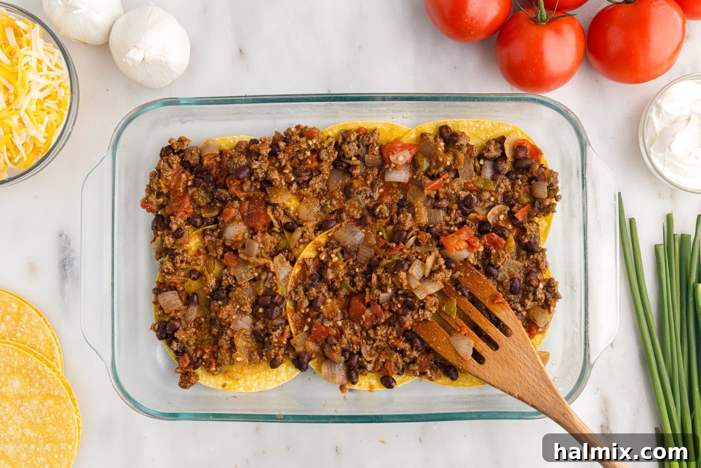 Spreading a layer of seasoned meat mixture smoothly over the corn tortillas, ensuring even coverage